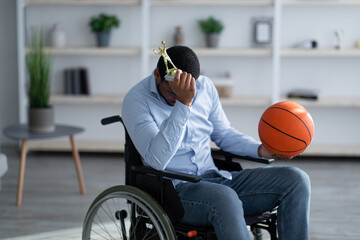 Young black basketball player in wheelchair holding ball and feeling stressed over his injury at home