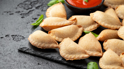 Margarita Margherita pizza parcels pockets filled with tomato, mozzarella cheese and basil served on black slate board with marinara sauce and olives. Party finger food
