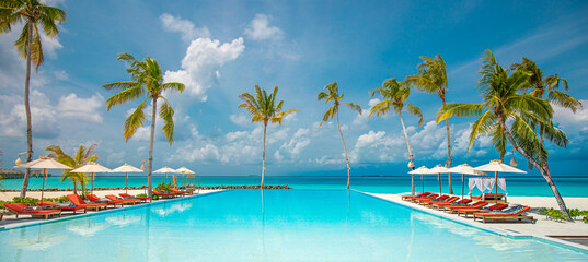 Relax tourism landscape. Luxurious beach resort with swimming pool and beach chairs or loungers leisure lifestyle, under umbrellas, palm trees, blue sky. Summer travel and vacation background concept