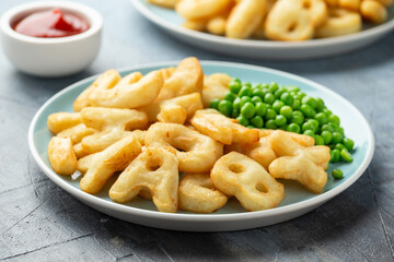 Alphabet potato fries snack with green peas and ketchup on plate. party food