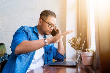 Close up of a asian man wears blue jeans jacket working, thinking and using laptop with white mockup screen in a coffee shop