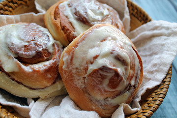 Cinnamon and cream buns lie on a cloth napkin on a wicker plate on a wooden table. The concept of baking for a delicious breakfast or dessert for a tea party. 