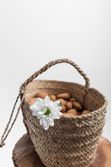 Fototapeta na wymiar closeup of a wicker basket adorned with a white flower and full of whole almonds on a wooden surface, the background is white and there is space for writing, vertical photo