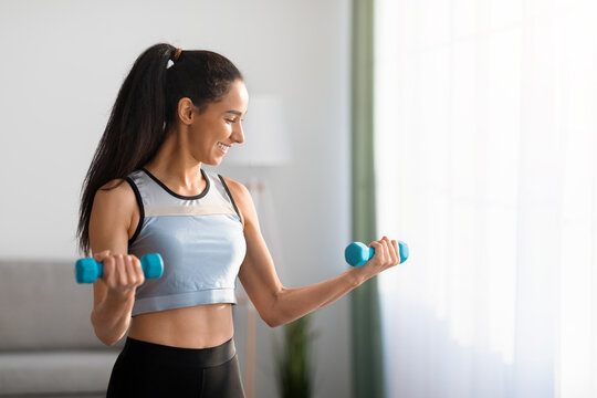 Closeup of positive young woman doing dumbbell workout at home