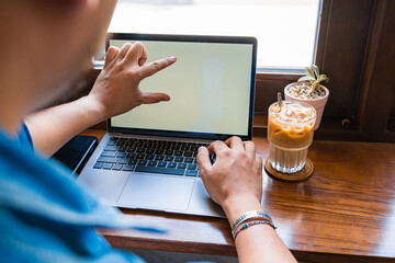 Close-up of male hands using laptop and smartphone at coffee shop with white mockup screen, man's hands typing on laptop keyboard, side view of a man using computer in cafe