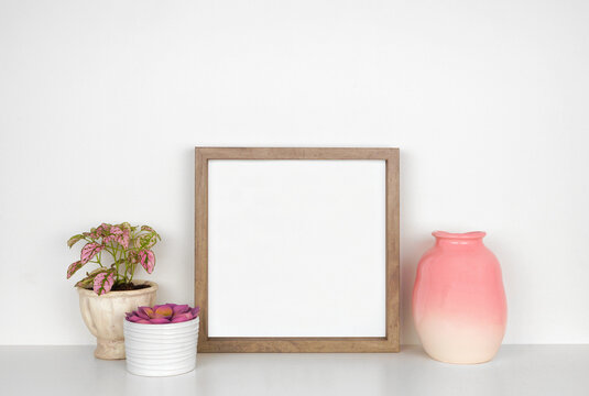 Mock up wood square frame with pink houseplants and vase. White shelf against a white wall. Copy space.