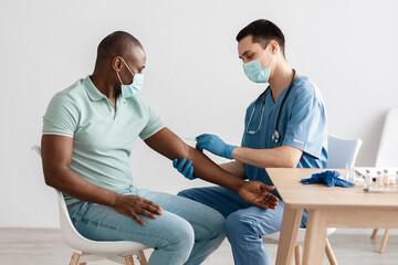Obraz premium Millennial doctor in protective mask and uniform gives shot to african american patient in clinic