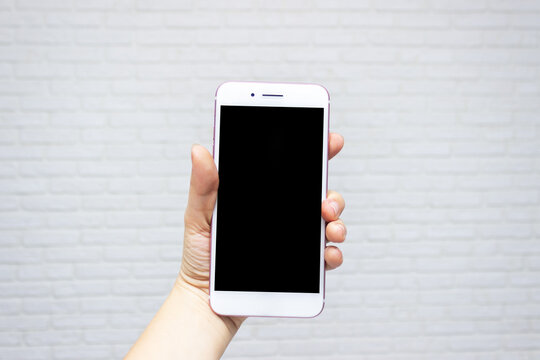 Template for the design. White phone with black screen in female hand on white brick wall