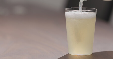 Man pour ginger beer into tumbler glass on walnut table