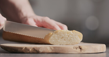 man hand slicing baguette on olive wood board
