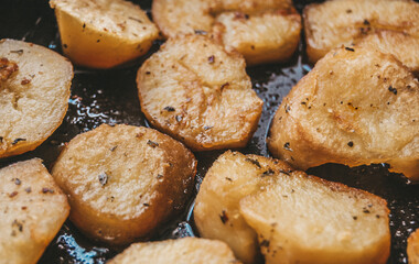 Macro photo of golden yellow roasted potatoes with herbs and spices at cast iron pan. Home cooking.
