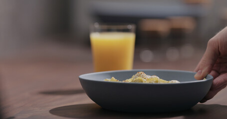 man put blue bowl with pesto fettuccine on walnut table with orange juice