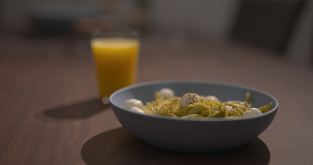blue bowl with pesto fettuccine on walnut table with orange juice