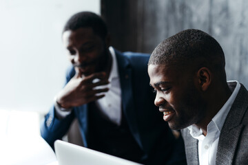 Serious african american men at conference talking to each other while sitting at the table and working at the laptop