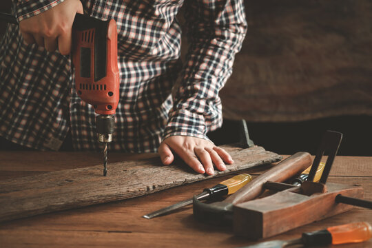 Carpenter drills a hole with an electrical drill, carpentry and woodwork tools on wooden background, capenter working table, Vintage.