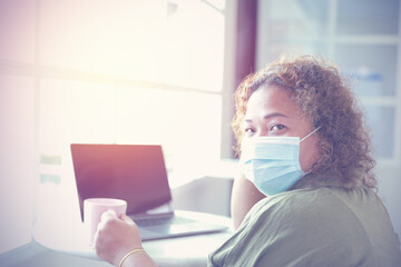 Asian business woman wearing medical mask left hande holding pink coffee cup looking at camera. Concept Social distances, work from home. At present, there is a outbreak of the coronavirus.