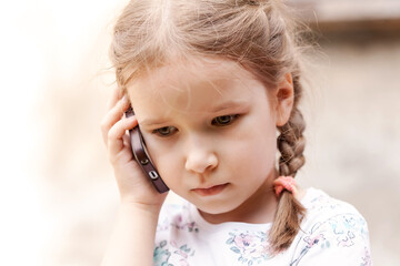 Young child, little school age girl talking on the phone, holding her modern smartphone next to her ear, portrait, face extreme closeup. Phone call concept, children and telecommunication, lifestyle
