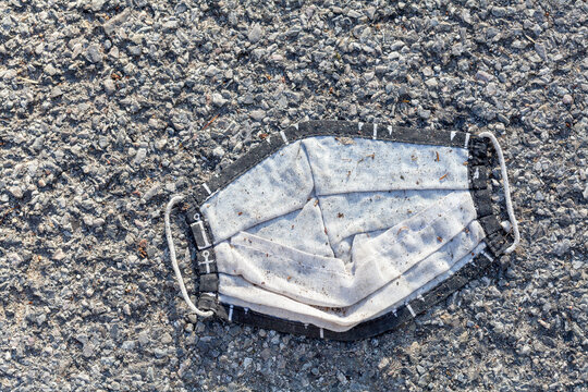 Abandoned old trampled dirty used protective face mask thrown, laying on the ground, left behind on concrete, object closeup, top view. Covid 19, corona virus epidemic symbol, pandemic ending concept