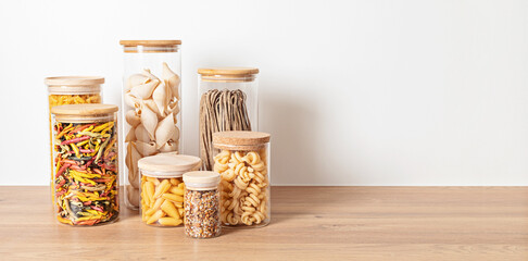 Assortment of italian traditional pasta in glass jars on wooden table. Healthy balanced food, sustainable lifestyle, zero waste eco friendly concept. Banner