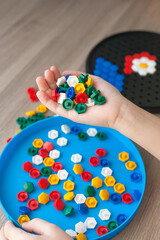 Childrens hands put the details of colored mosaics into a drawing of flowers on the table. Leisure of the child in confinement. Table game. Top view
