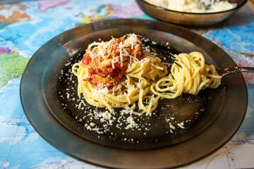 Boiled spaghetti with tomato and grated cheese on brown glass plate.
