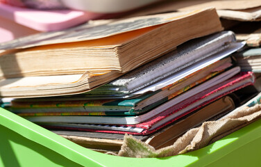 Lots of different old books and paper notebooks in a container outside in sunlight, stack. Box full of old literature, giving away used books. Book fairs, antiques, moving abstract concept, nobody