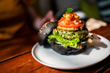 Broccoli quinoa charcoal burger topped with guacamole, mango salsa and fresh salad served on a white plate. Creative vegan meal for vegetarians.