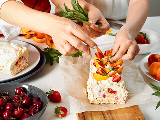 Meringue roll with a delicate air cream, mint and fruit filling of strawberries and peaches. Pavlova summer sweet dessert. Summer baking. Copy space. Mom and daughter prepare meringue roll.