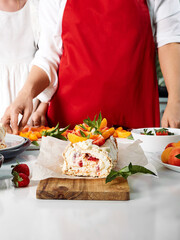 Meringue roll with a delicate air cream, mint and fruit filling of strawberries, peaches and mint. Pavlova summer sweet dessert. Berry dessert on the background of a woman. Summer baking. Copy space.