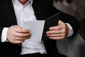 the groom holds an envelope with a letter from the bride. man is reading and sitting in the chair near the window. A letter for the groom. declaration of love.