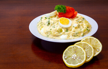 Gaucho mayonnaise, potato salad in white dish on wooden table, with slices of lemon. Selective focus