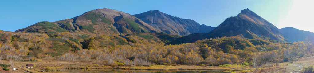 Naklejka premium Panorama view of the lake and the Vachkazhets mountain range. High mountains against the background of an autumn forest with yellow leaves and a lake. Kamchatka Peninsula, Russia.