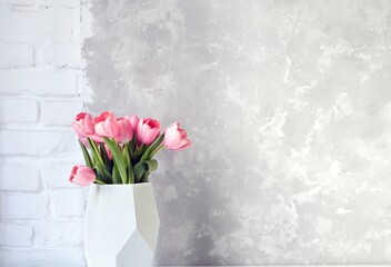 Pink tulip bouquet in vase on white table on white brick wall and bright concrete background. Copy space for text.
