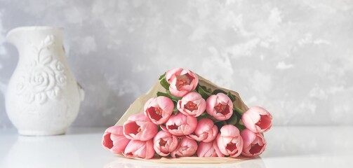 Bouquet of fresh pink tulips on white table with vase on the background. Copy space for text.