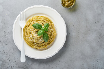 Pasta spaghetti with pesto sauce and fresh basil leaves in white bowl. Grey background.  Mock up. Top view.