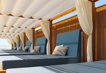Cabana style relaxation lounge furniture deck chairs loungers under wooden pergola with white...