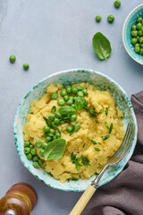 Mashed potato with butter, green peas, onions, basil in a white bowl on a light slate, stone or concrete background. Top view with close up.
