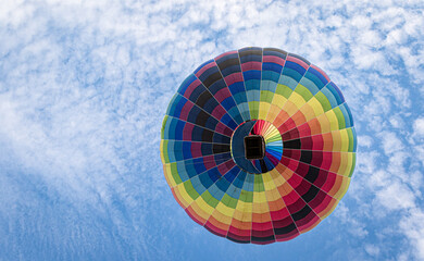 Ein Heißluftballon als bunter Punkt genau von unten gegen den blauen Himmel mit weißen Wölkchen...