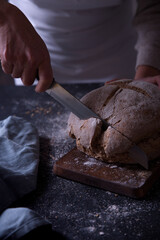 Hands slicing fresh bread, on dark background.