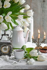 A bouquet witte tulips in a vase, a white alarm clock en kopje koffie op witte tafel. traditional English tea, high tea	