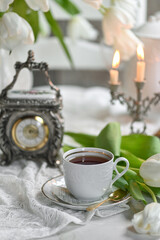 A bouquet witte tulips in a vase, a white alarm clock en kopje koffie op witte tafel. traditional English tea, high tea	