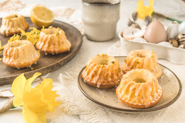 Homemade delicious mini lemon bundt cakes (muffins) on a plate on a easter table with fresh spring blossoms.