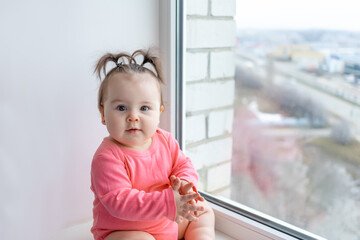 the baby sits on the window sill and looks at the camera