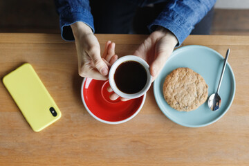 top view of a modern man in a coffee shop holding a red cup of coffee or tea and eating cookies yellow smartphone