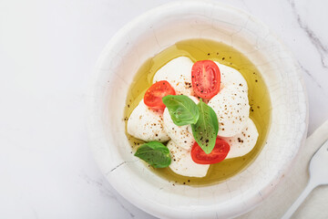 Caprese salad. Mozzarella cheese with basil and cherry tomato in white ceramic plate and tomato cherry on slate stone background, copy space. Mock up.