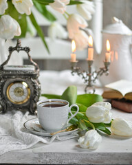 Obraz na płótnie Canvas A bouquet witte tulips in a vase, a white alarm clock en kopje koffie op witte tafel. traditional English tea, high tea 