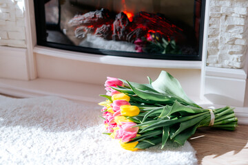 Fresh spring yellow and pink tulips bouquet on the fur carpet floor by the fireplace with copy space for text. Love, easter, International Women, Mother and Happy Valentine day concept