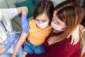 Female doctor vaccinating child patient at home. Coronavirus, Covid-19 concept.