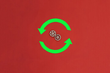 Two round green arrows, two wooden gears on a red background. Change, movement.
