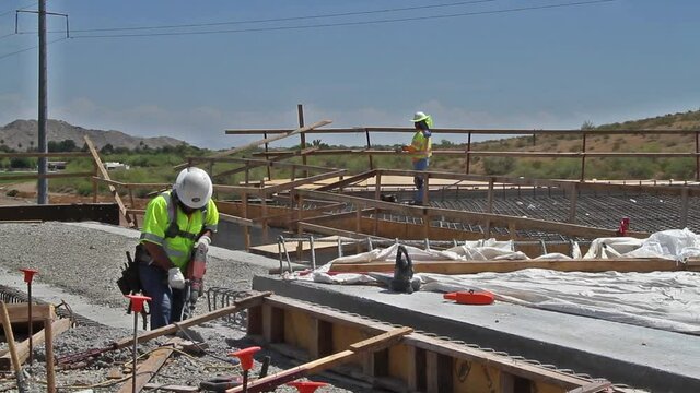 Jack-Hammer operator trimming concrete with rebar inspector in background on bridge building project